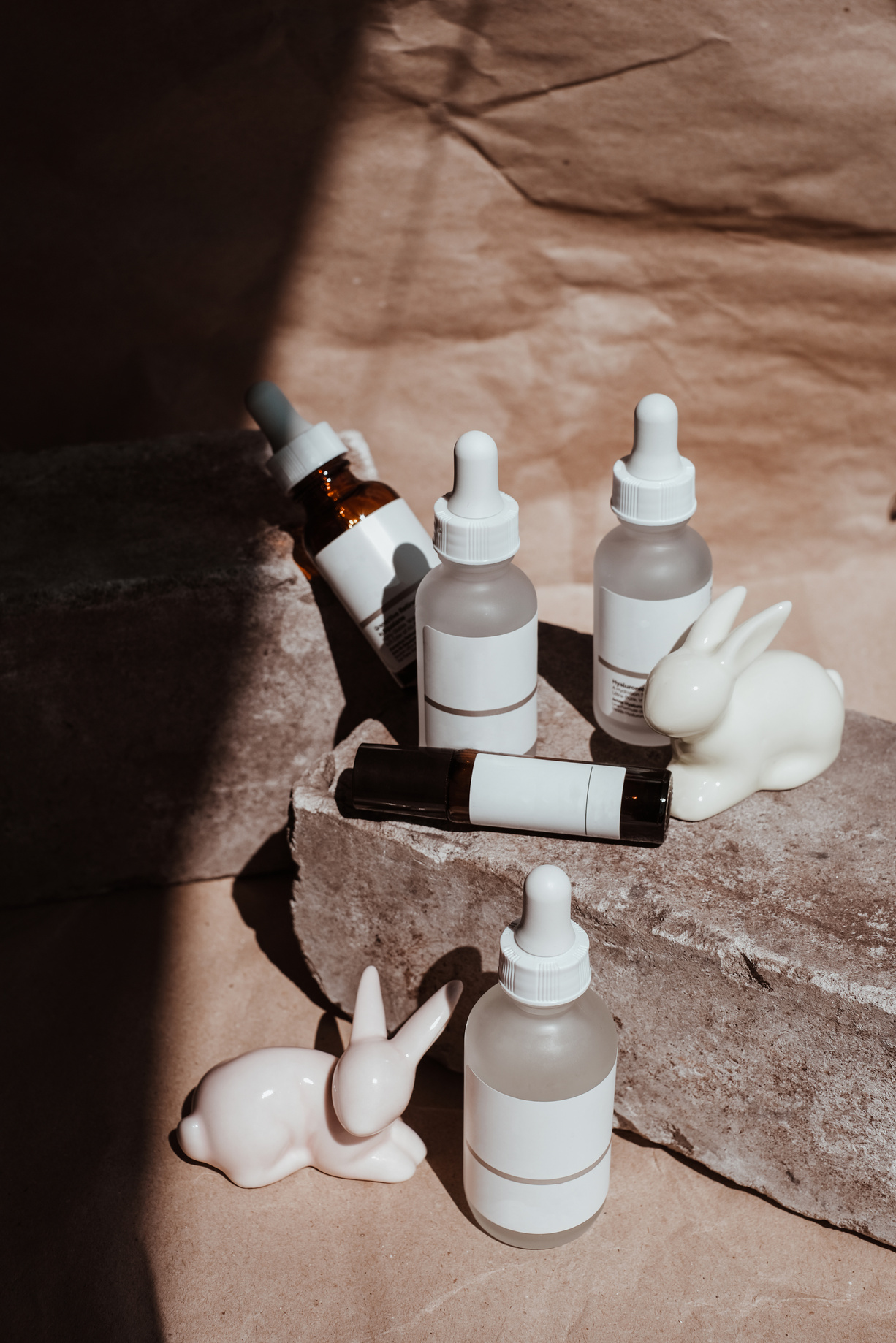 Bottles of Cosmetic Products on Rock with White Ceramic Rabbits